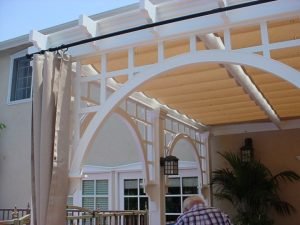 White trellis cover with tan slide wire awning and custom drapes